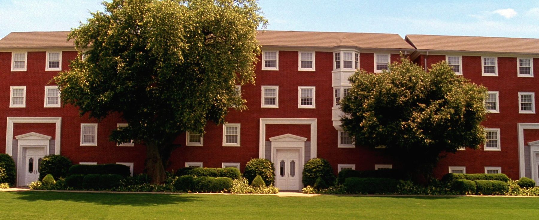 Three-storey red brick apartment blocks set behind a hedge and lawn in Fresh Meadows, Queens
