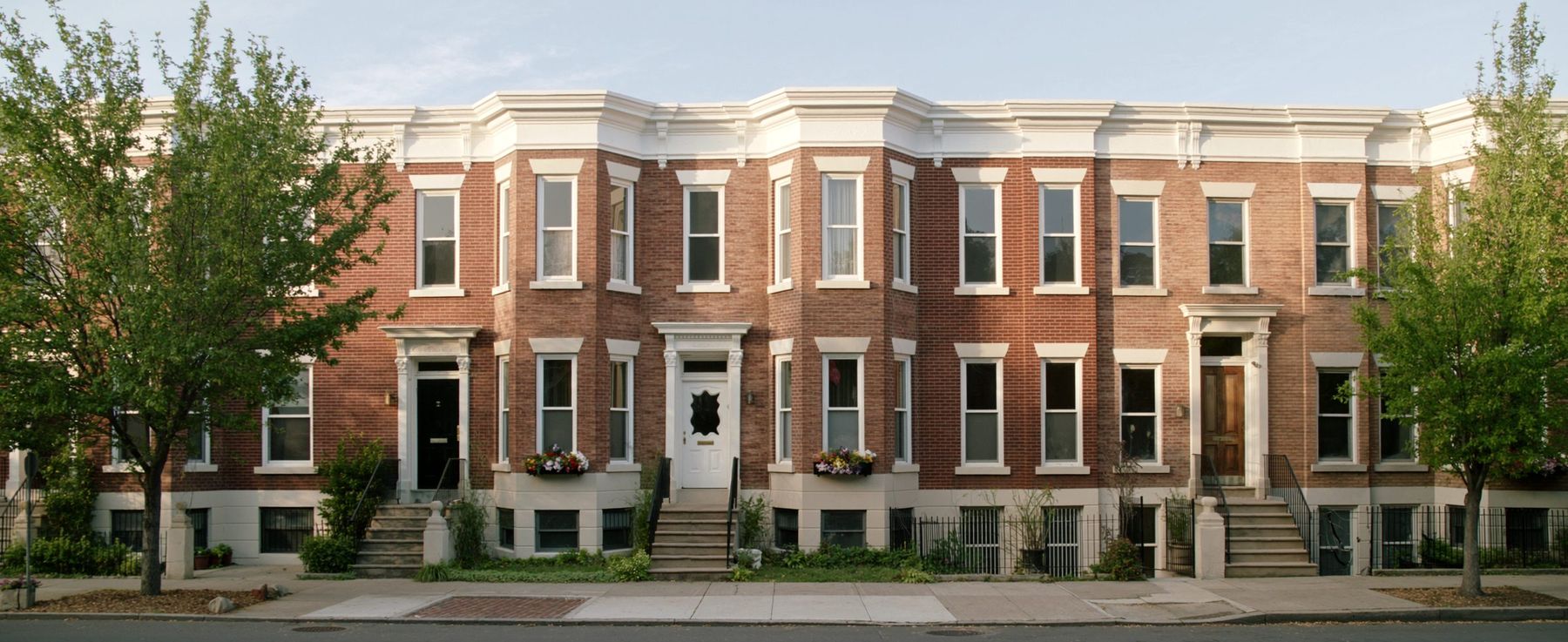 Brick row houses with bay windows below an elevated subway trestle in Woodside, Queens