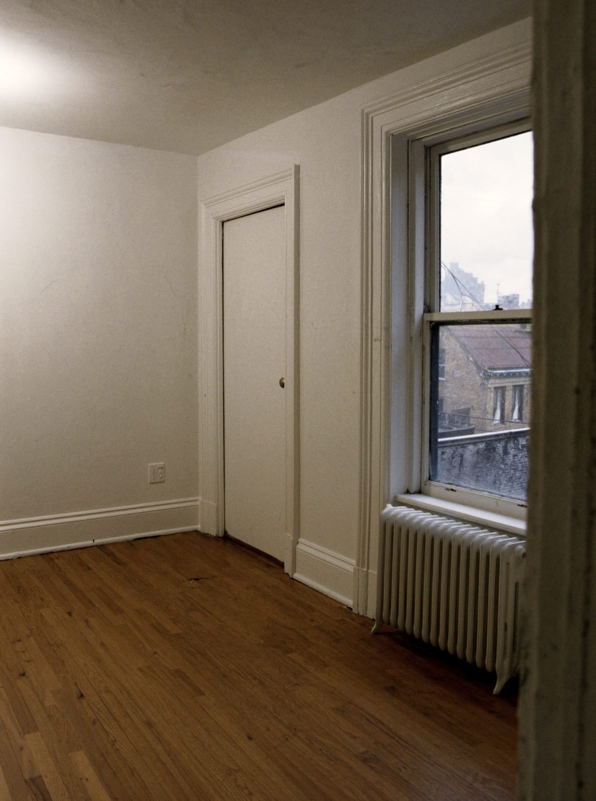 A vacant apartment in an older Queens building, with refinished floors, a tall window and a cast-iron radiator