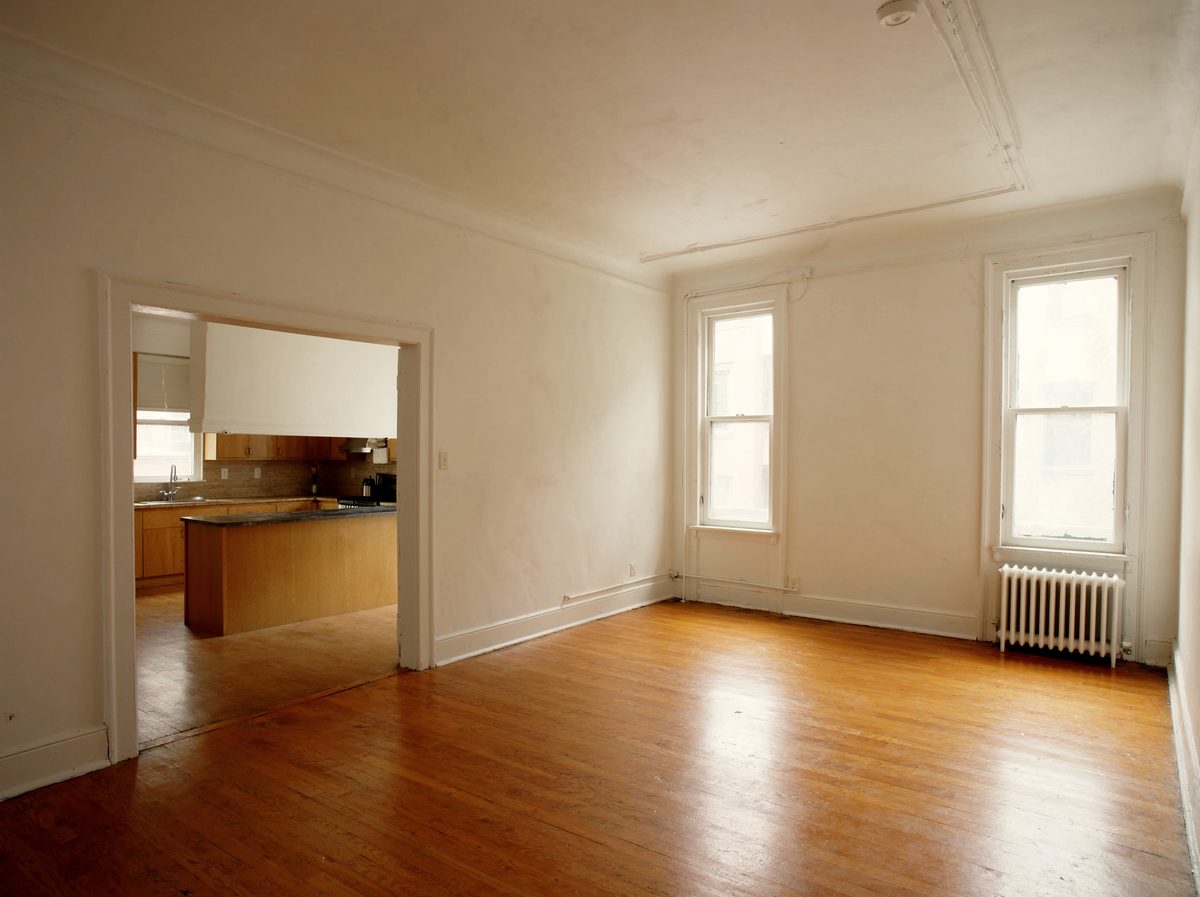 A bright empty one-bedroom living room with hardwood floors and tall windows